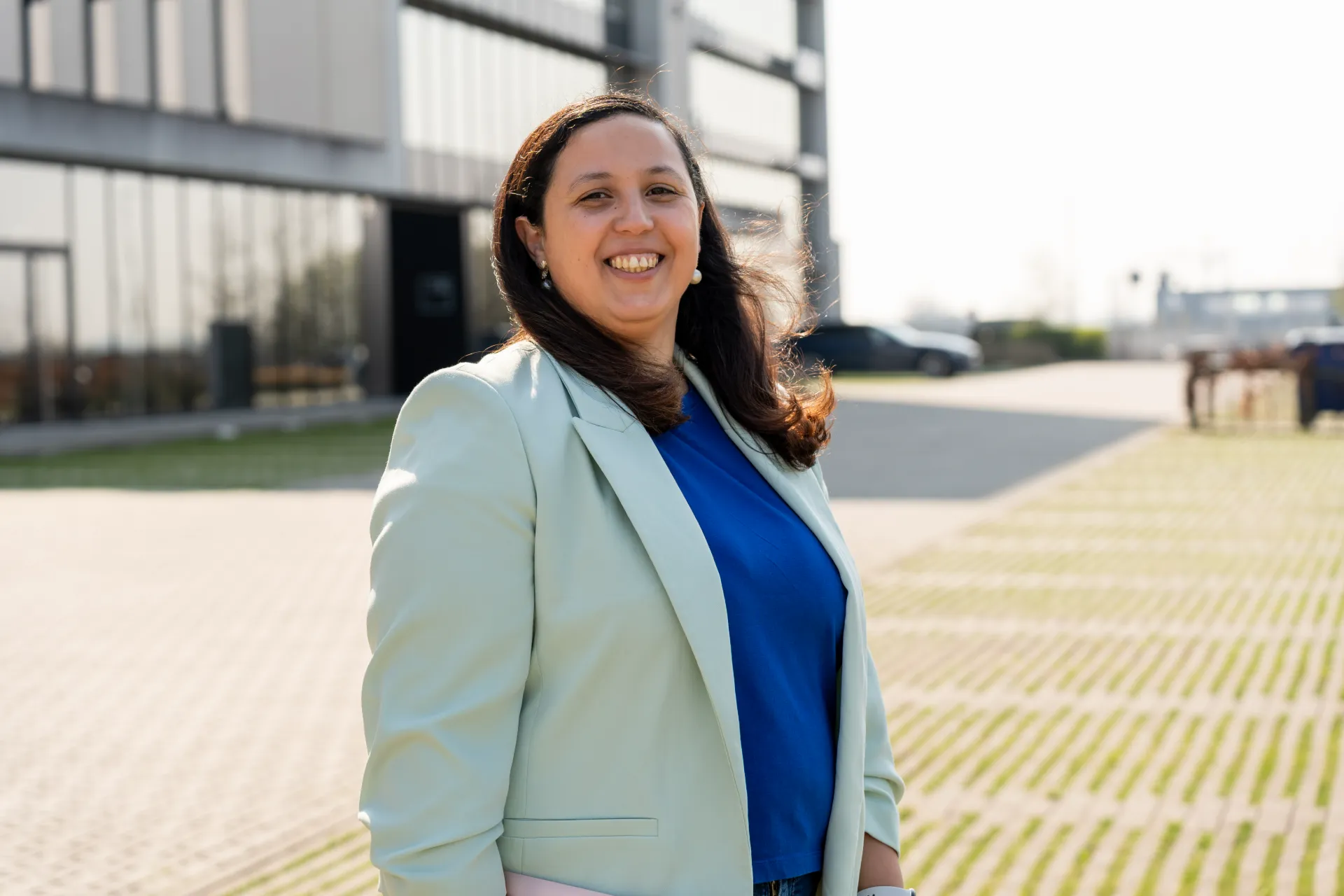 Lachende financieel adviseur Samra Daoud met lichte blazer buiten voor modern kantoorgebouw.