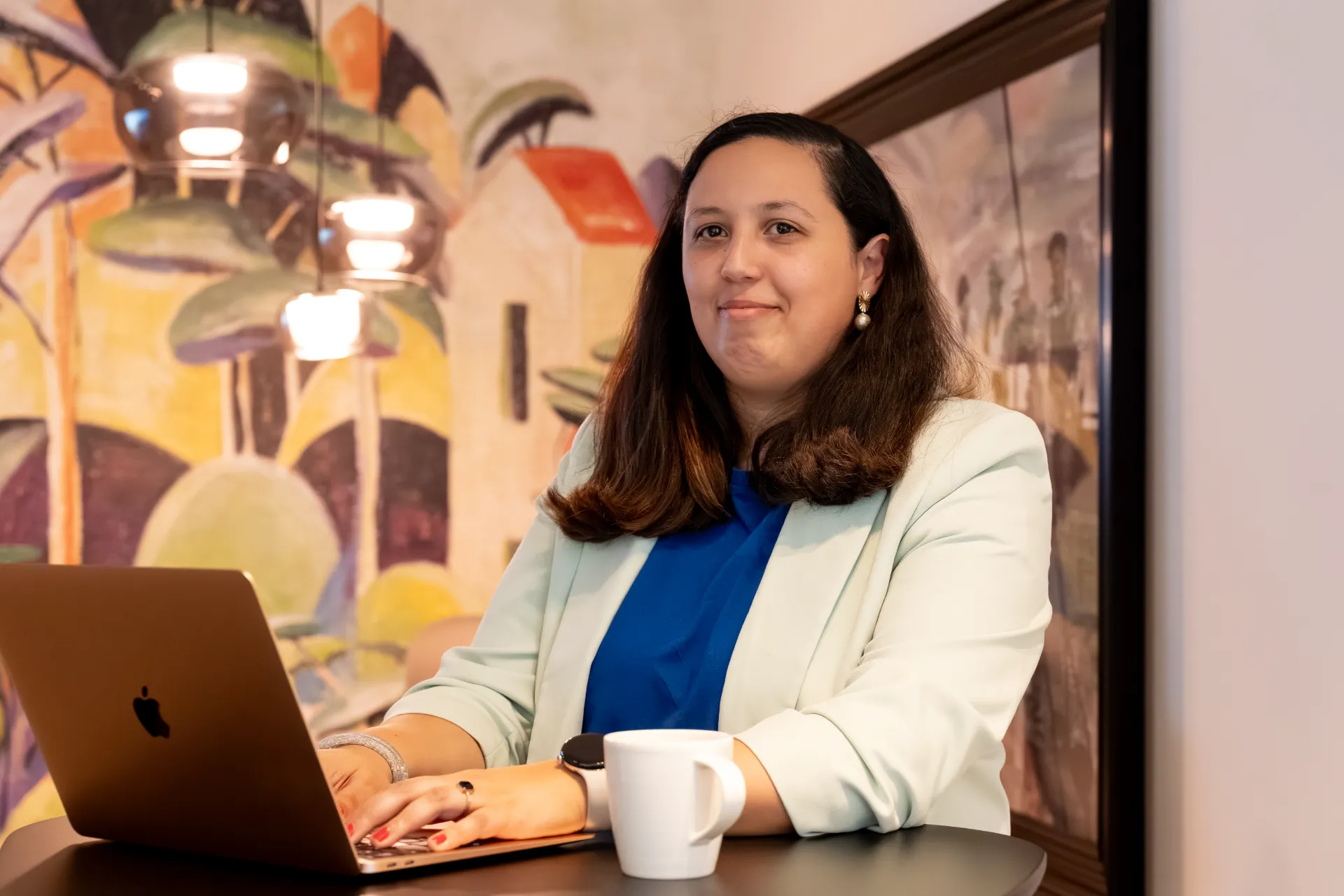 Samra Daoud, financieel adviseur, zit glimlachend aan een tafel met een laptop in een modern kantoor.